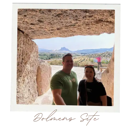A man and a woman standing in a cave with a blue sky background behind them at the cave entrance.