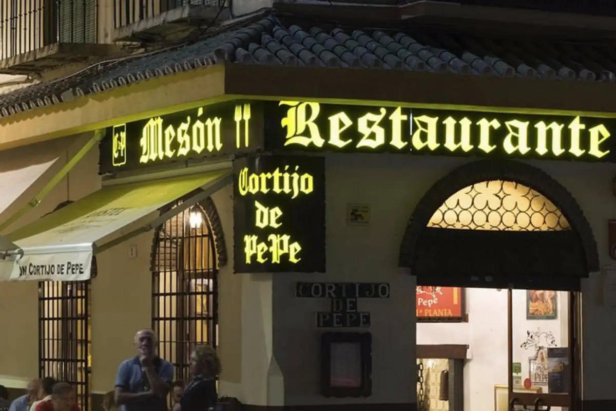 A neon sign reading Meson Restaurante viewed from the street in Malaga.