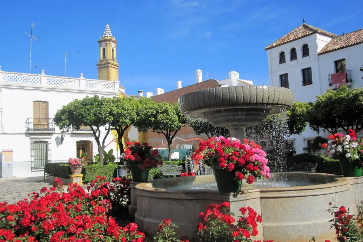 flowers lining a fountain in plaza de las flores in Estepona with buildings and a church in the background