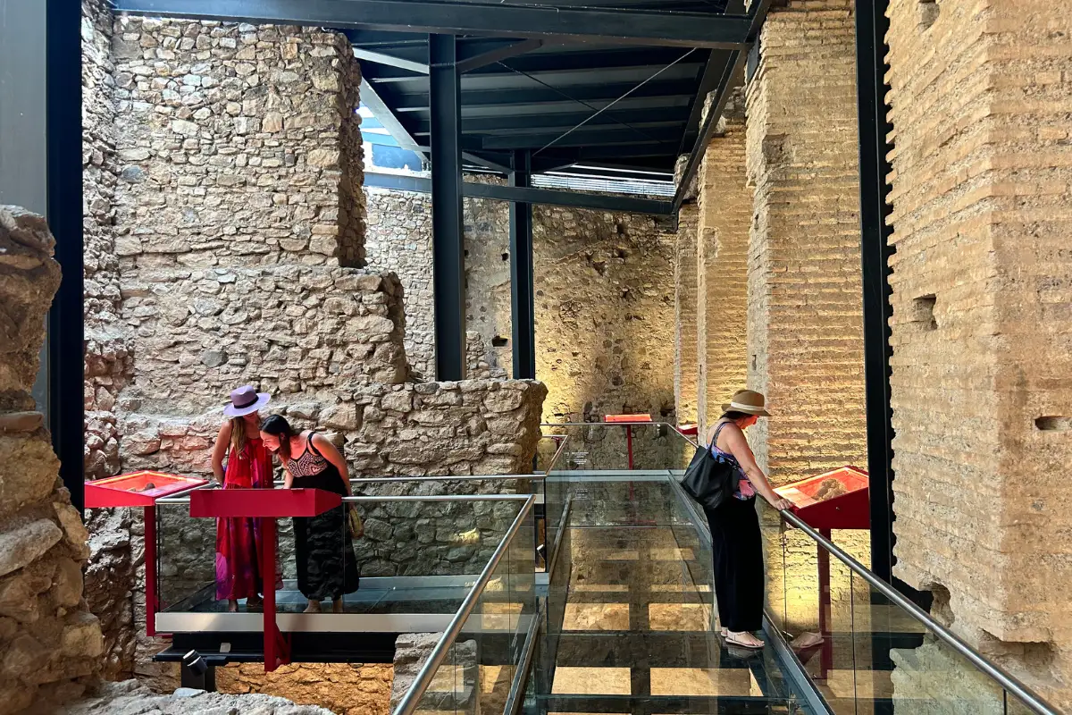 A glass walkway inside of the San Luis castle ruins with people looking at the exhibits.