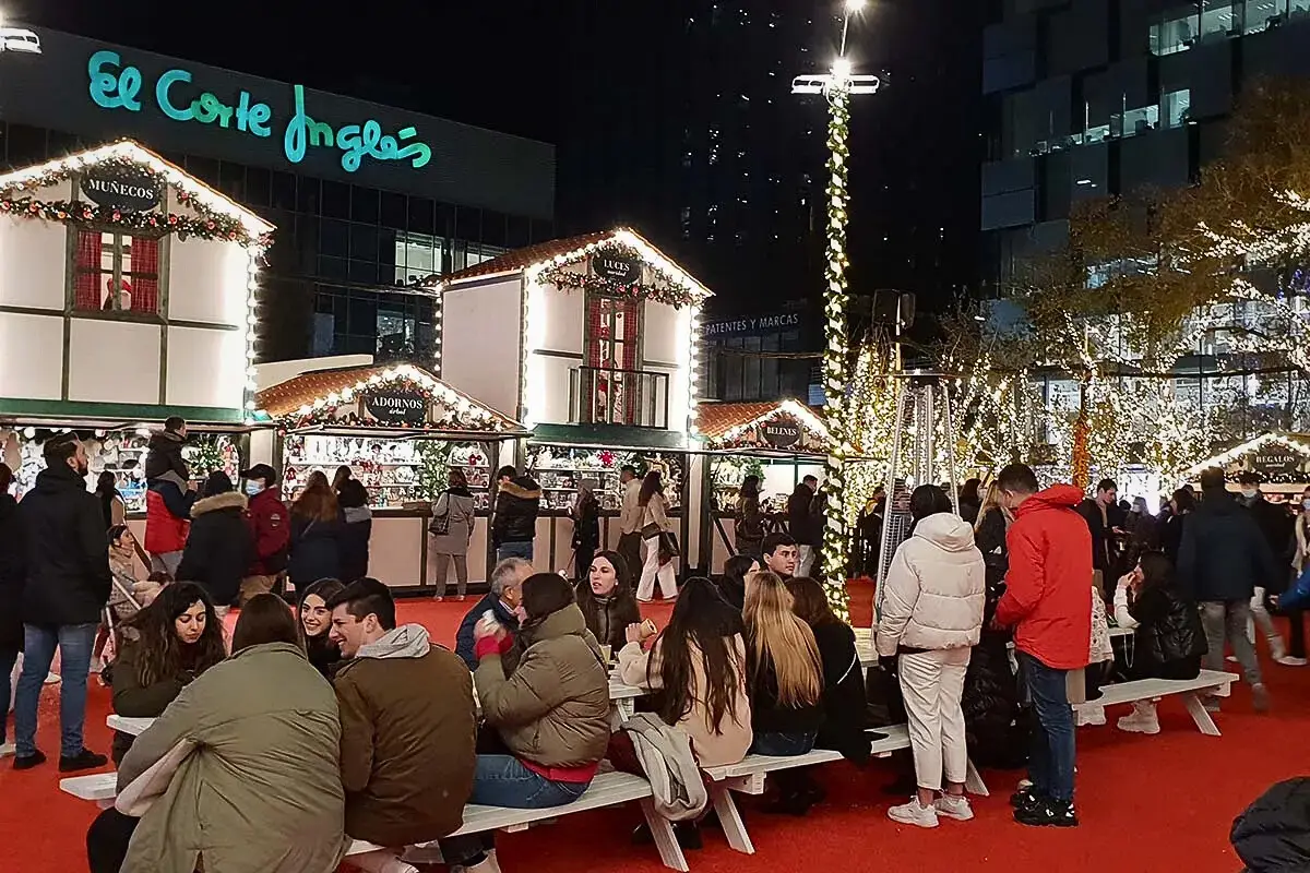 People sitting at neches with stalls in the background during Christmas at the El Coret Ingles market.