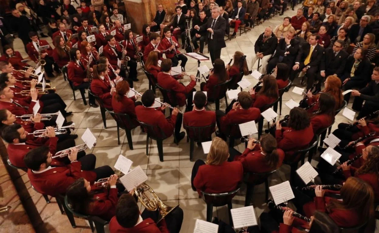 The Malaga municipal band is seated and playing music in a crowded hall.