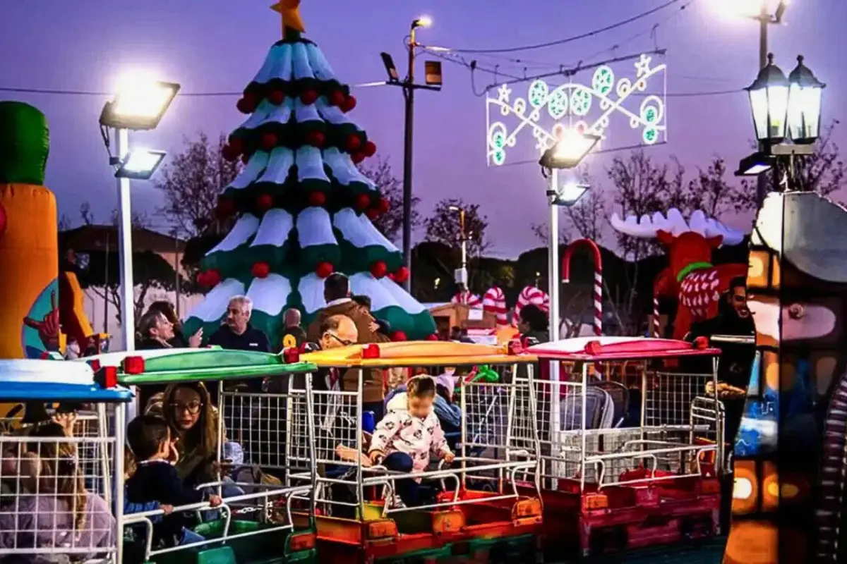 Children on a miniature train ride with a Christmas tree and parents in the background.